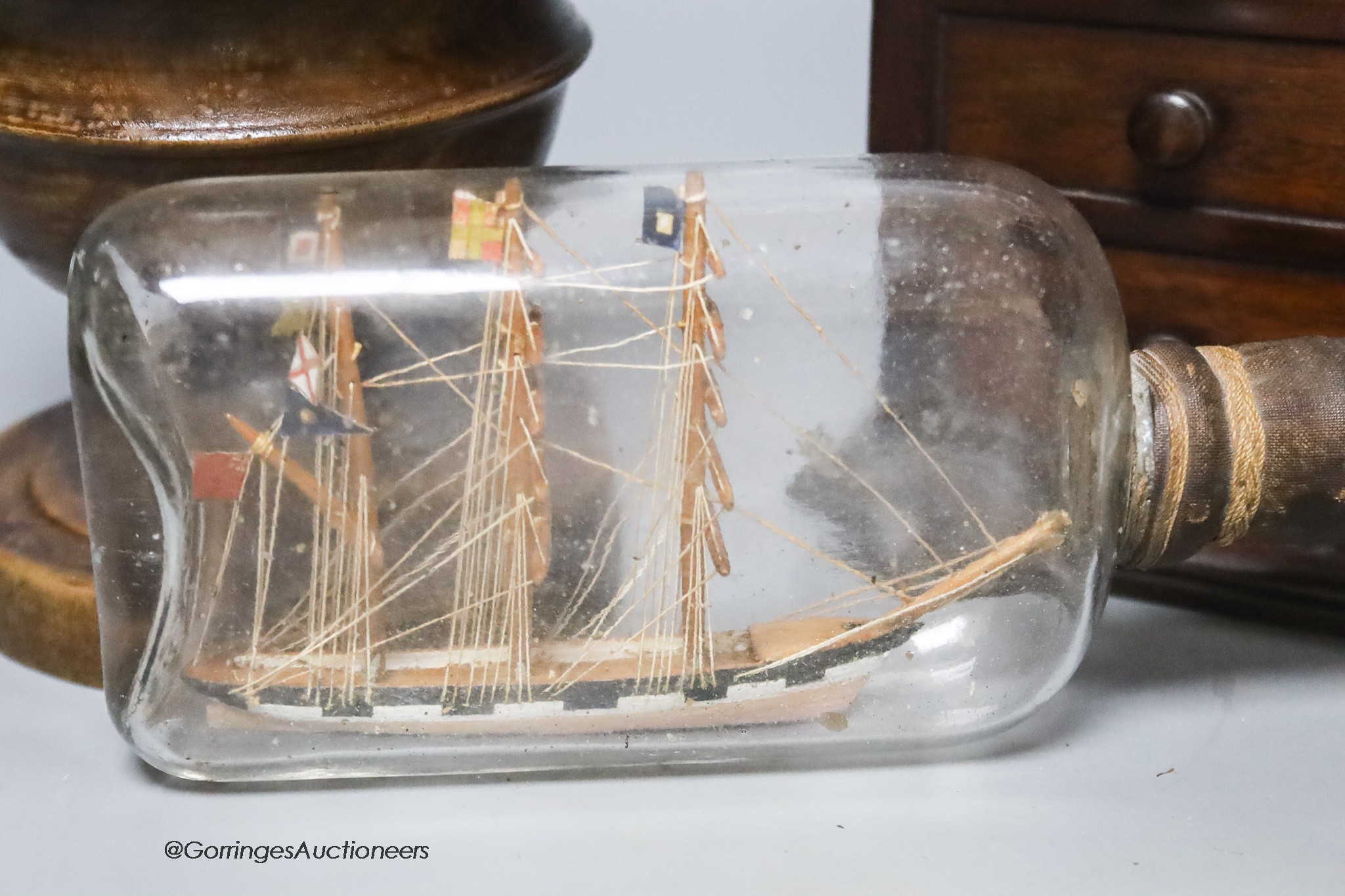 A Victorian mahogany 'chest of drawers' money bank, a turned wood bowl and cover and a small ship in a bottle, tallest 19cm